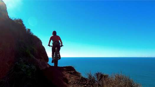 Silhouette of mountain biker on narrow trail above the ocean