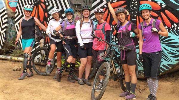 Group of women with mountain bikes in front of colorfully painted water tanks