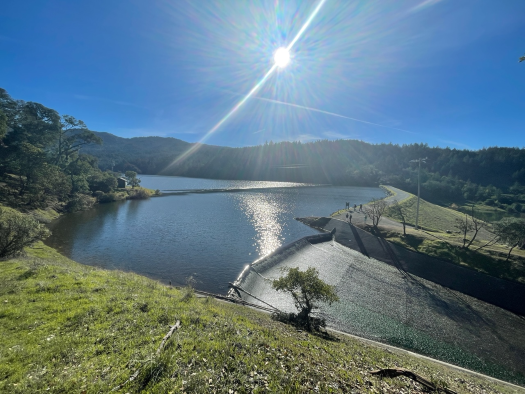 Sun shining over reservoir, with water flowing over spillway